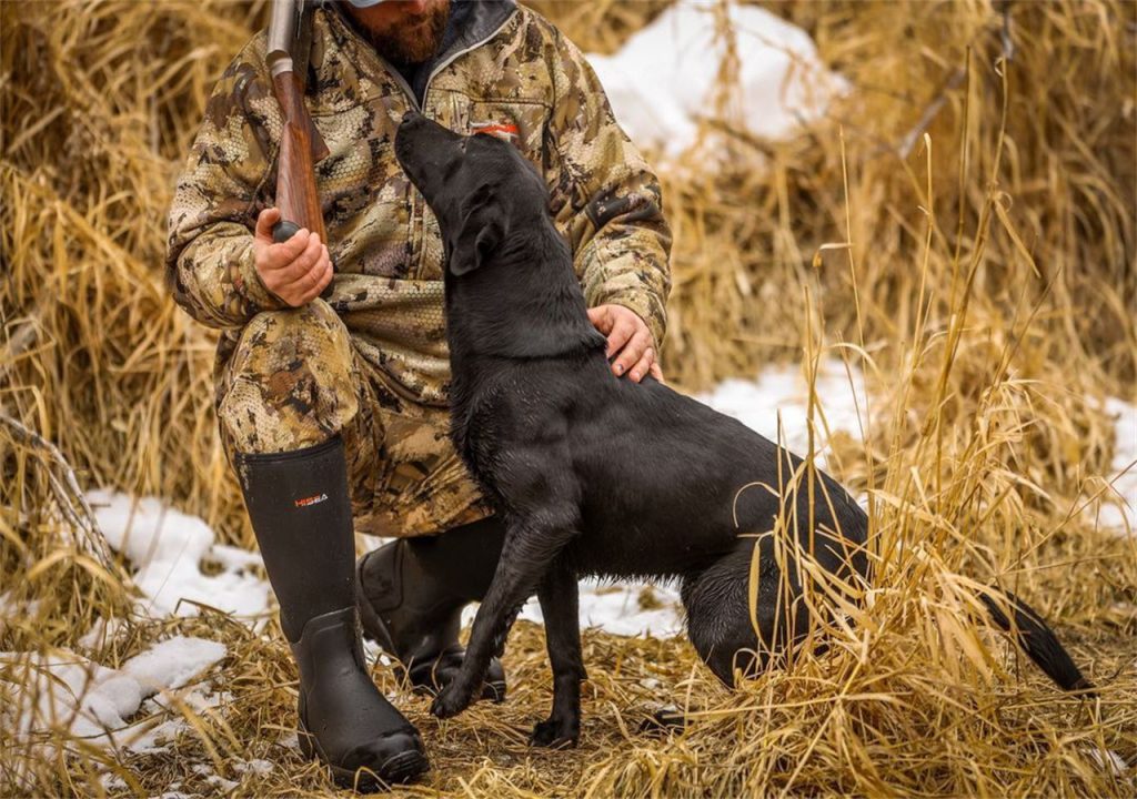  A man who is wearing HISEA boots is playing with his dog.