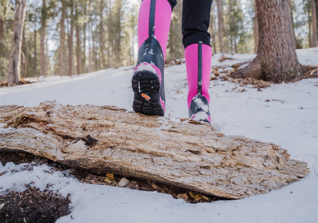 A woman in snow boots steps over a tree trunk, wearing HISEA snow boots.