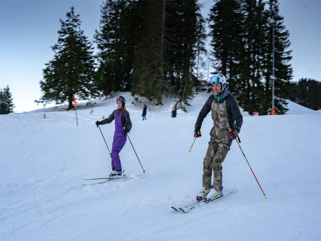 2 people wearing HISEA overall are skiing on a snowy mountain.