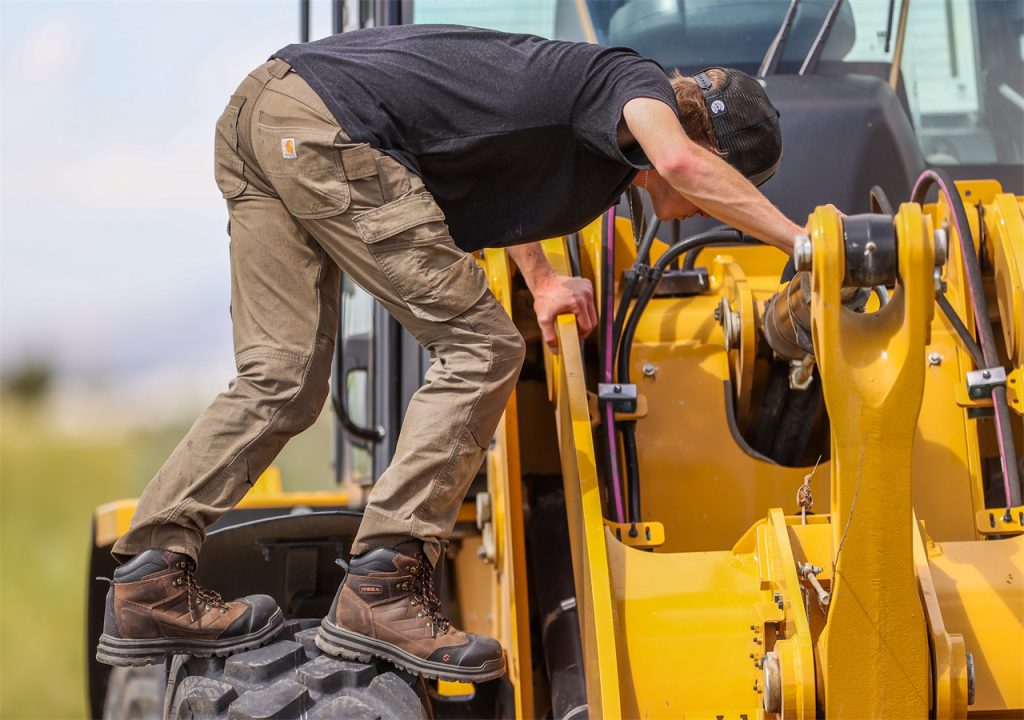 A young man wearing a peaked cap is working on a tractor.